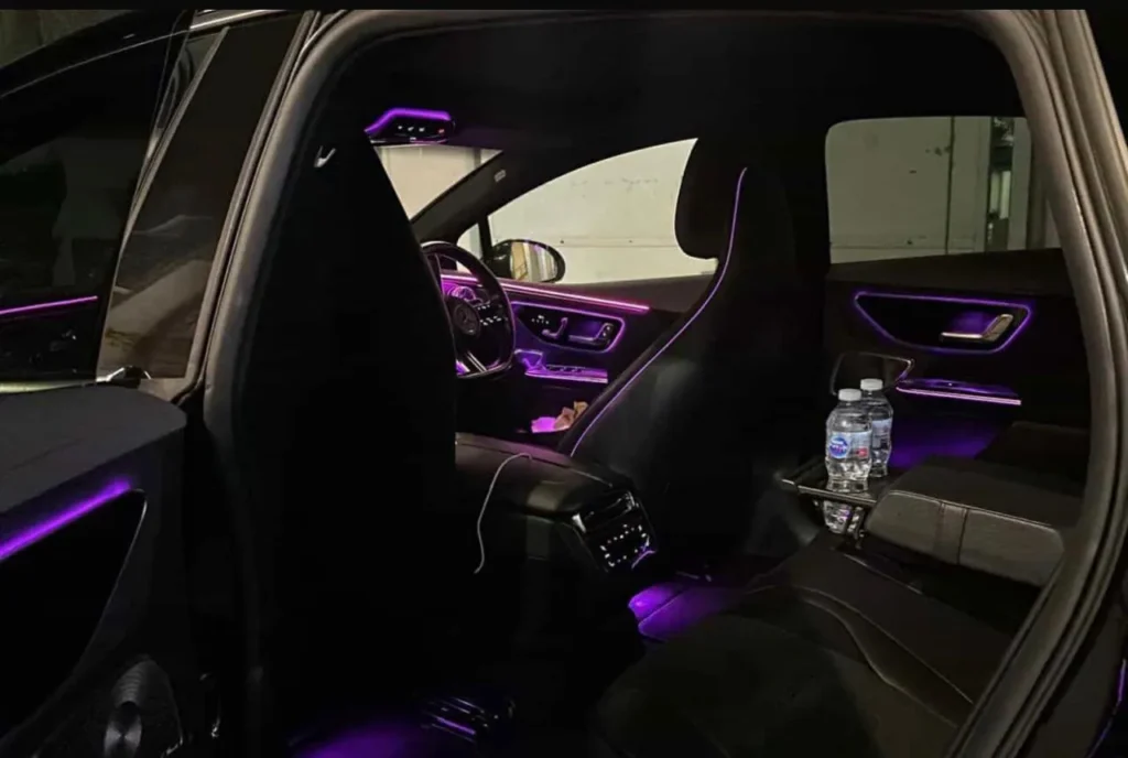 Luxury Mercedes chauffeur car rear cabin with black leather seats, purple ambient lighting and complimentary bottled water